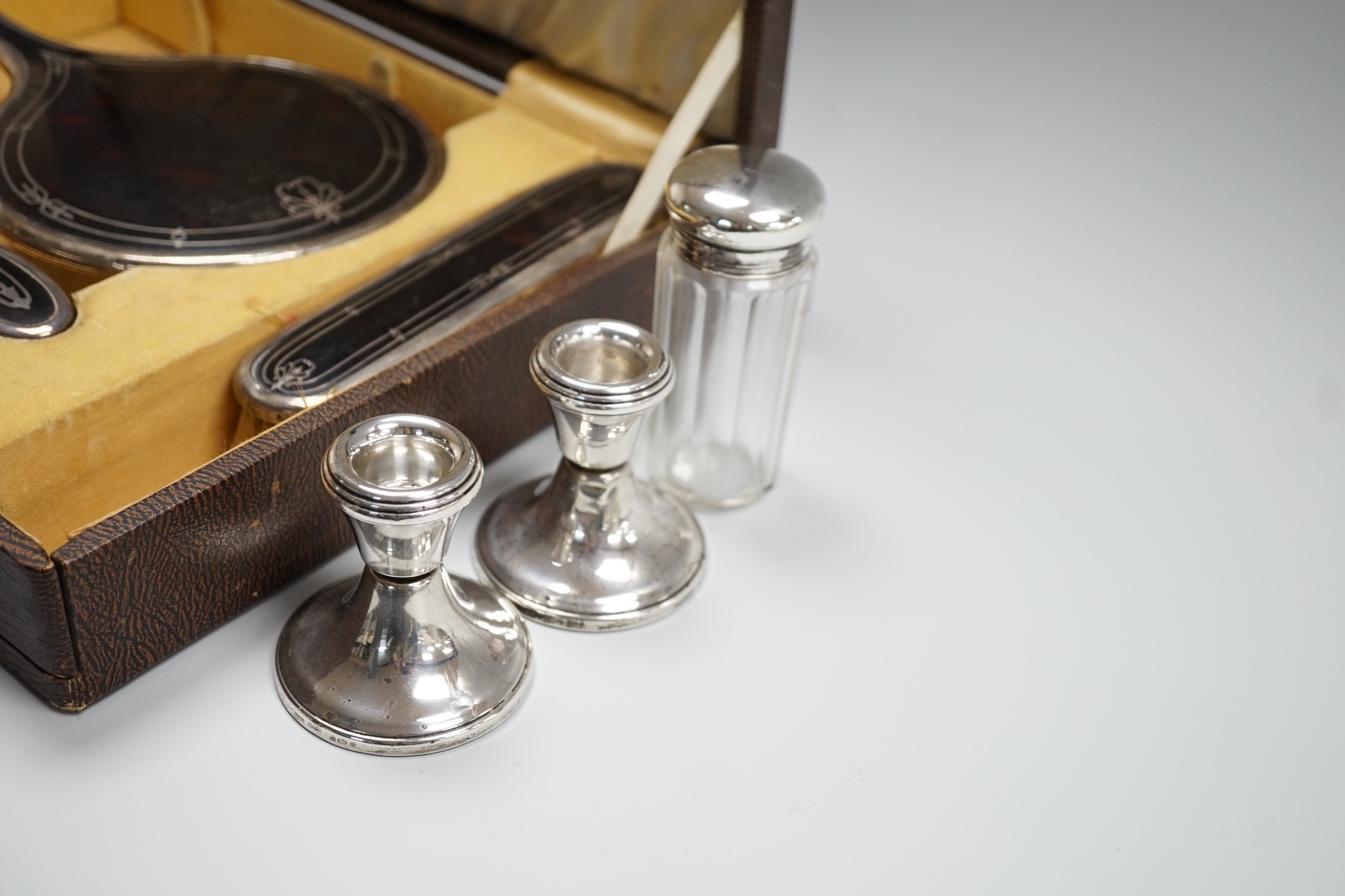 A George V cased three piece silver and tortoiseshell pique mounted mirror and brush set (lacking comb), Walker & Hall, Birmingham, 1931/37, a pair of modern silver mounted dwarf candlesticks and a silver mounted glass t